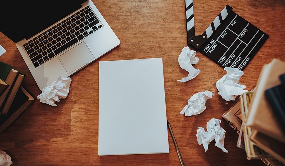 A blank page surrounded by crumpled up pieces of paper and a film clapperboard