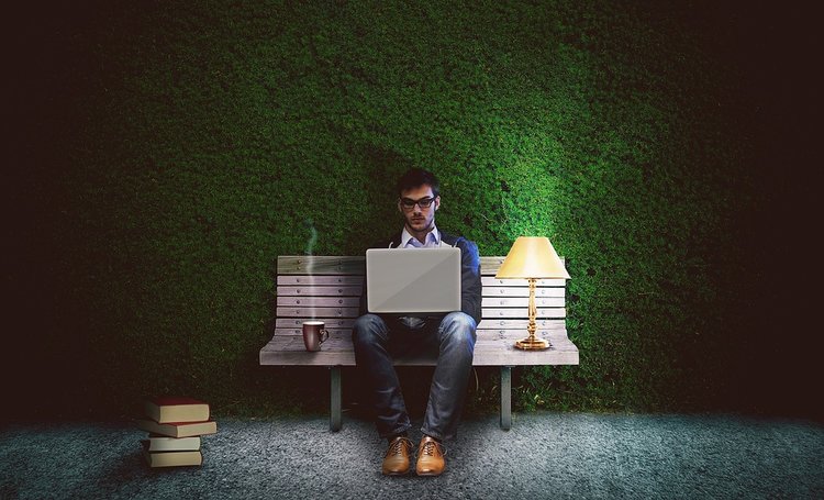 A man writing on a bench in a park